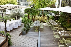 An outdoor dining area with multiple tables and chairs, surrounded by greenery and umbrellas. - La Maison Champs Elysées (Paris)