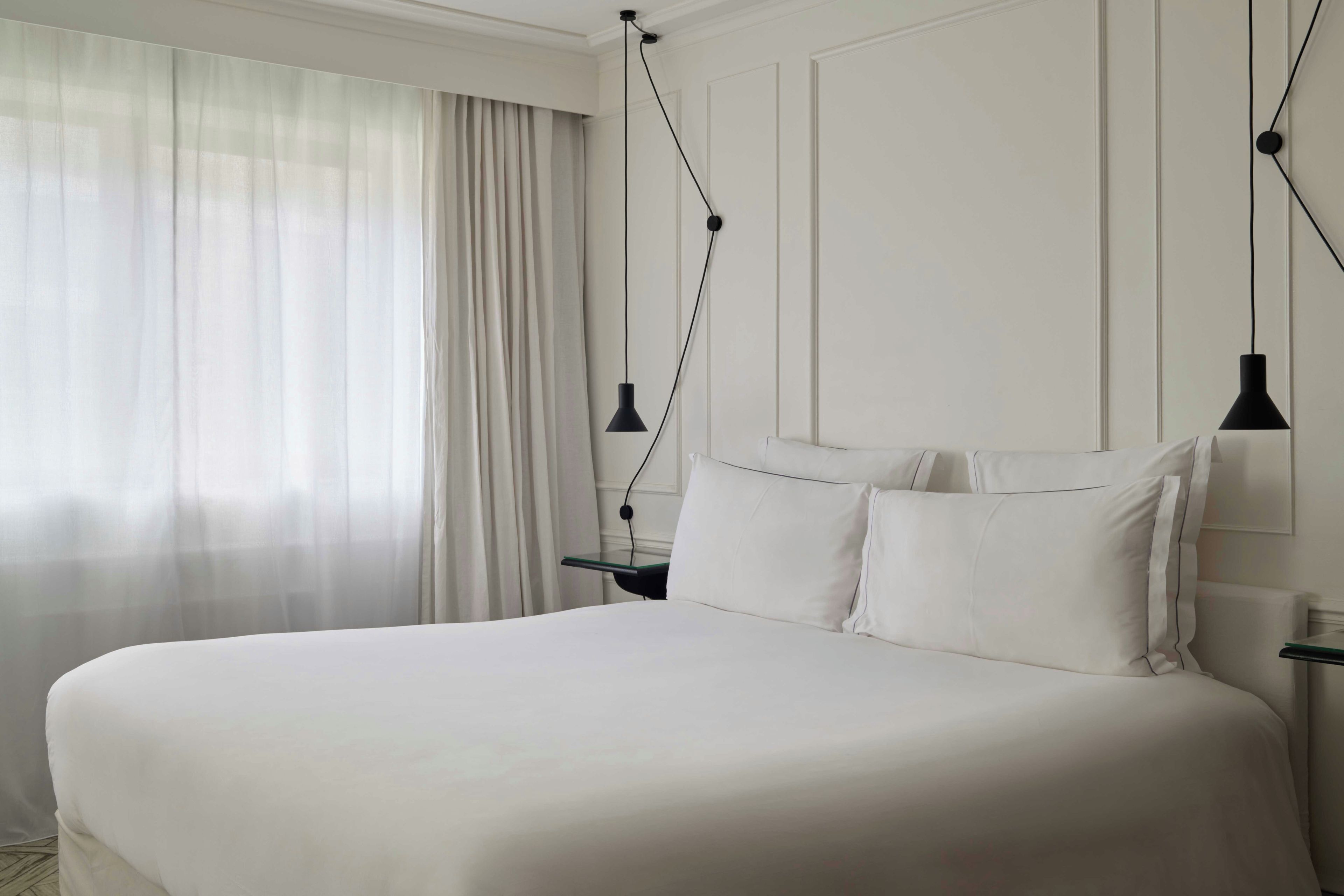 Una habitación de hotel con una cama grande, una mesita de noche, una lámpara y una ventana con cortinas.
