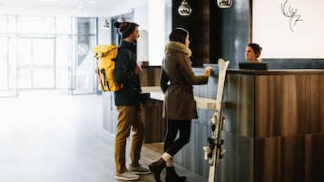 A reception area with a wooden reception desk, a coat rack with skis, and a person using a laptop.