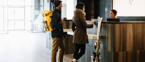 A reception area with a wooden reception desk, a coat rack with skis, and a person using a laptop.