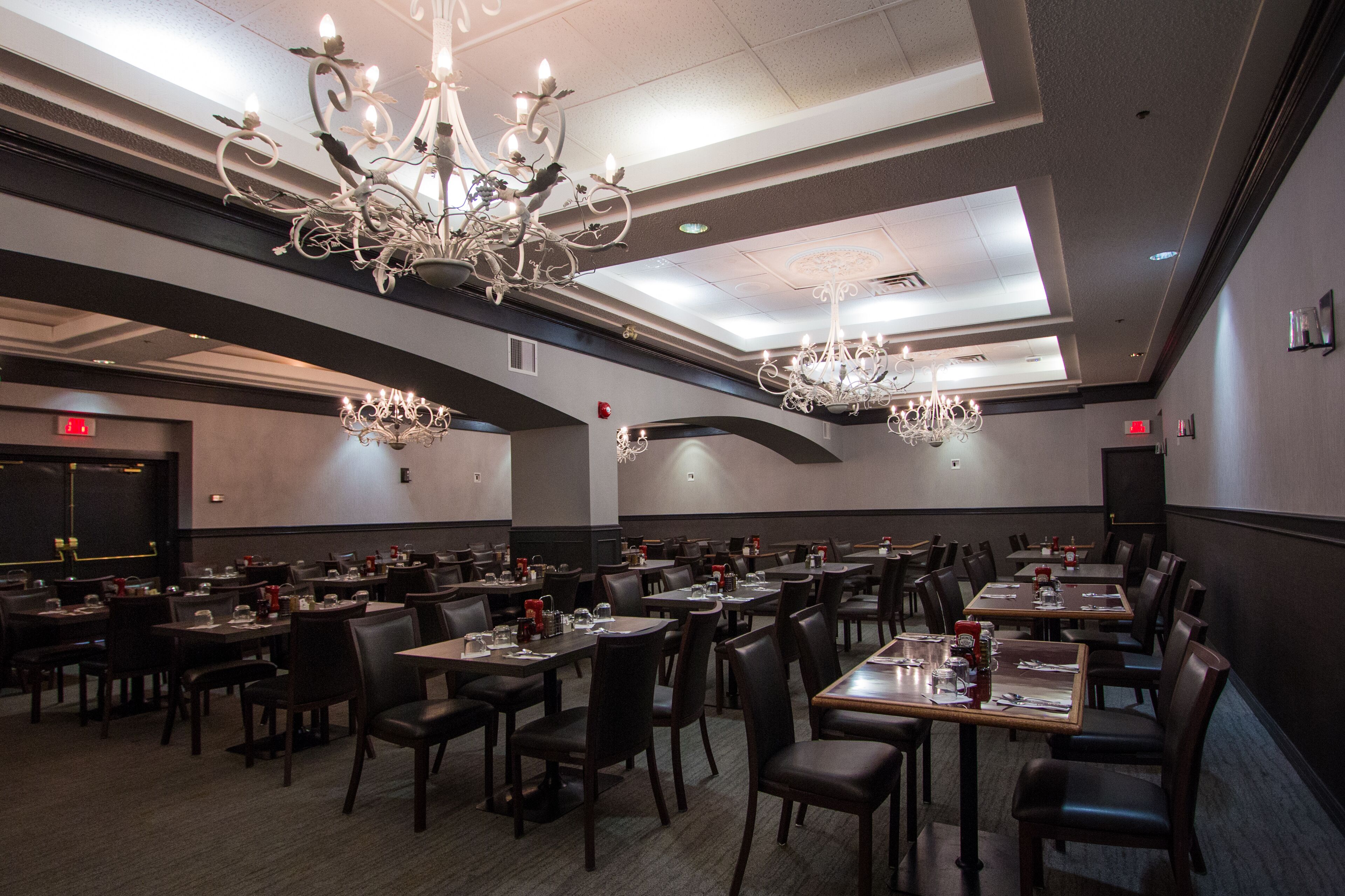 A spacious dining area with multiple tables and chairs, elegant chandeliers, and a modern ceiling design.