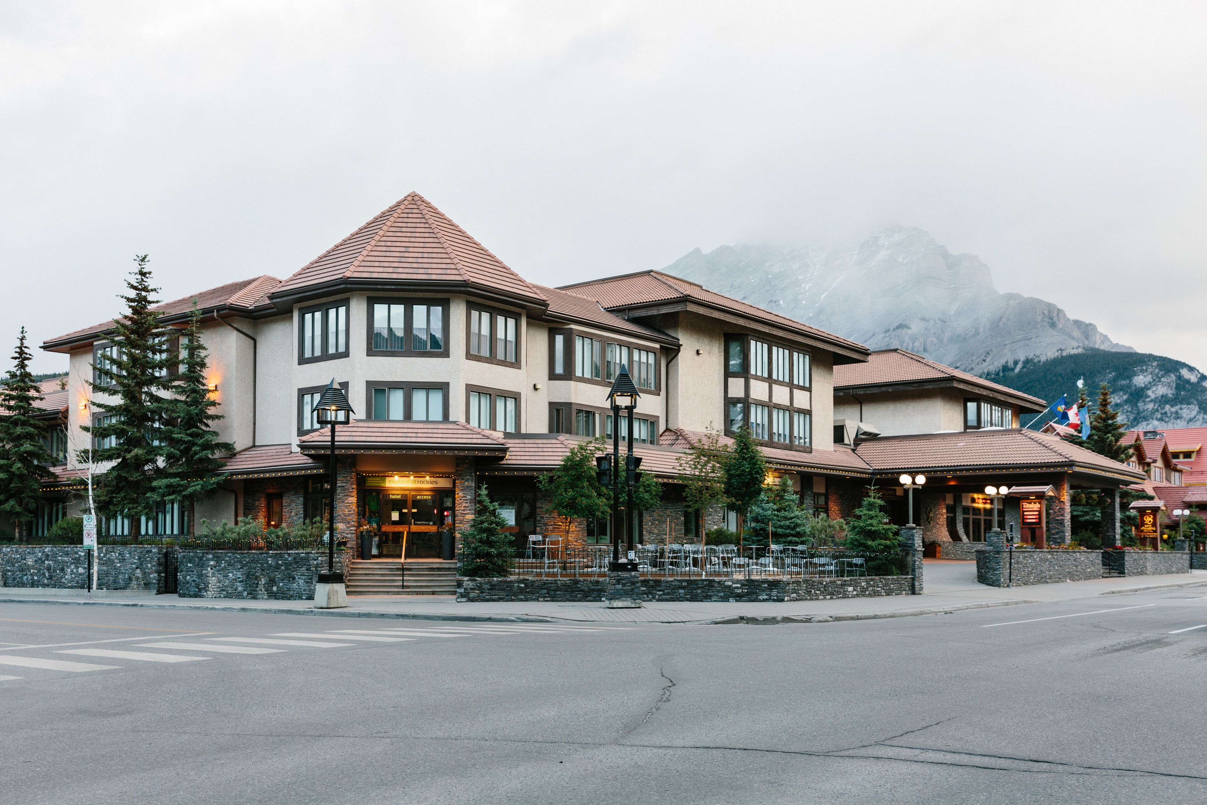 Un hotel de varios pisos con una entrada destacada en esquina, amplias ventanas y montañas al fondo.