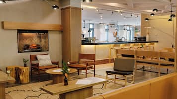 A modern hotel lobby with wooden furniture, a fireplace, and a bar area.