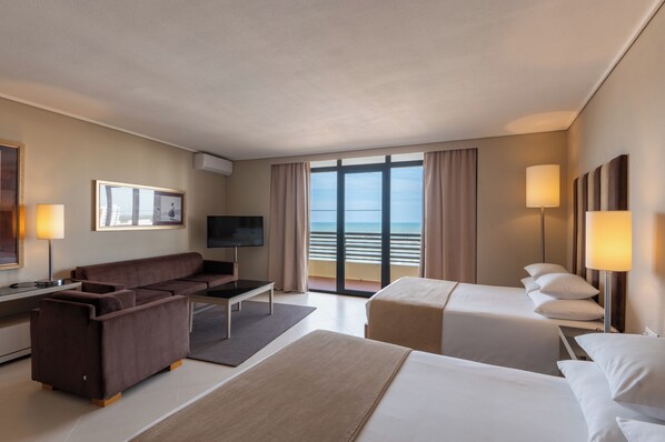 A hotel room with a sofa, a TV, a bed, and a view of the sea. - Vila Gale Ampalius Resort Hotel (Loulé)