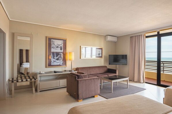 Habitación de hotel con cama, escritorio con lámpara, sofá, televisión y balcón con vistas.