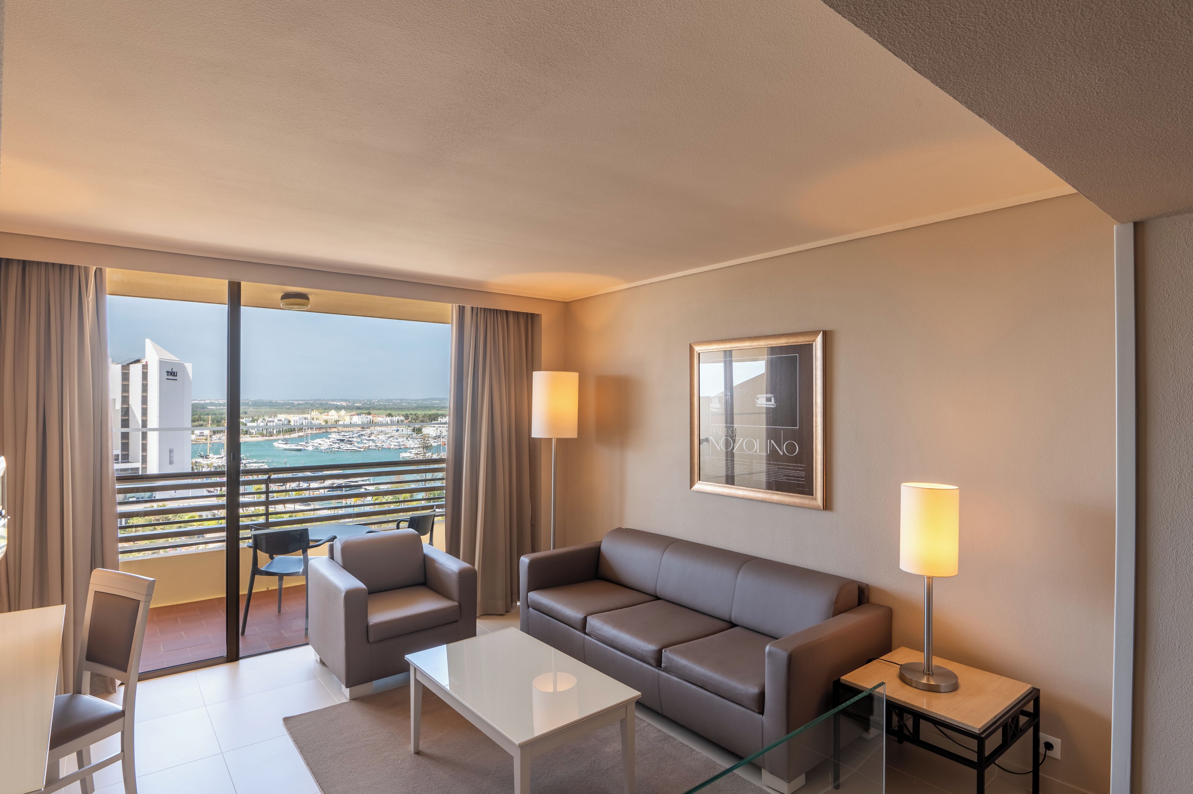 Une chambre d’hôtel avec un balcon, un canapé, une table basse et un fauteuil.