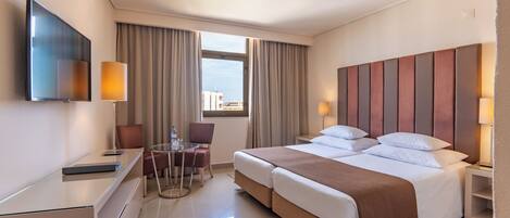 Habitación de hotel con cama, mesitas de noche, escritorio, silla, televisor y ventana con cortinas.