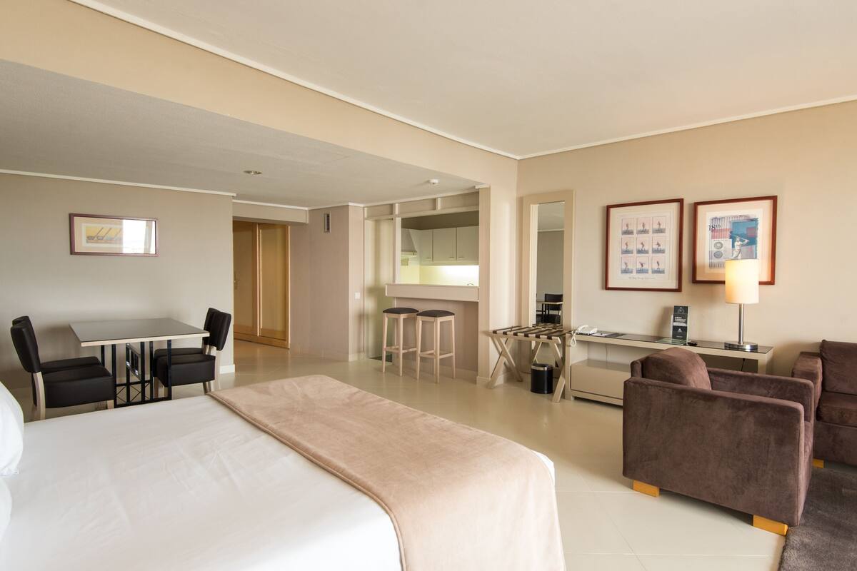 Ett hotellrum med en säng, ett skrivbord, en stol, en soffa och en liten köksdel.