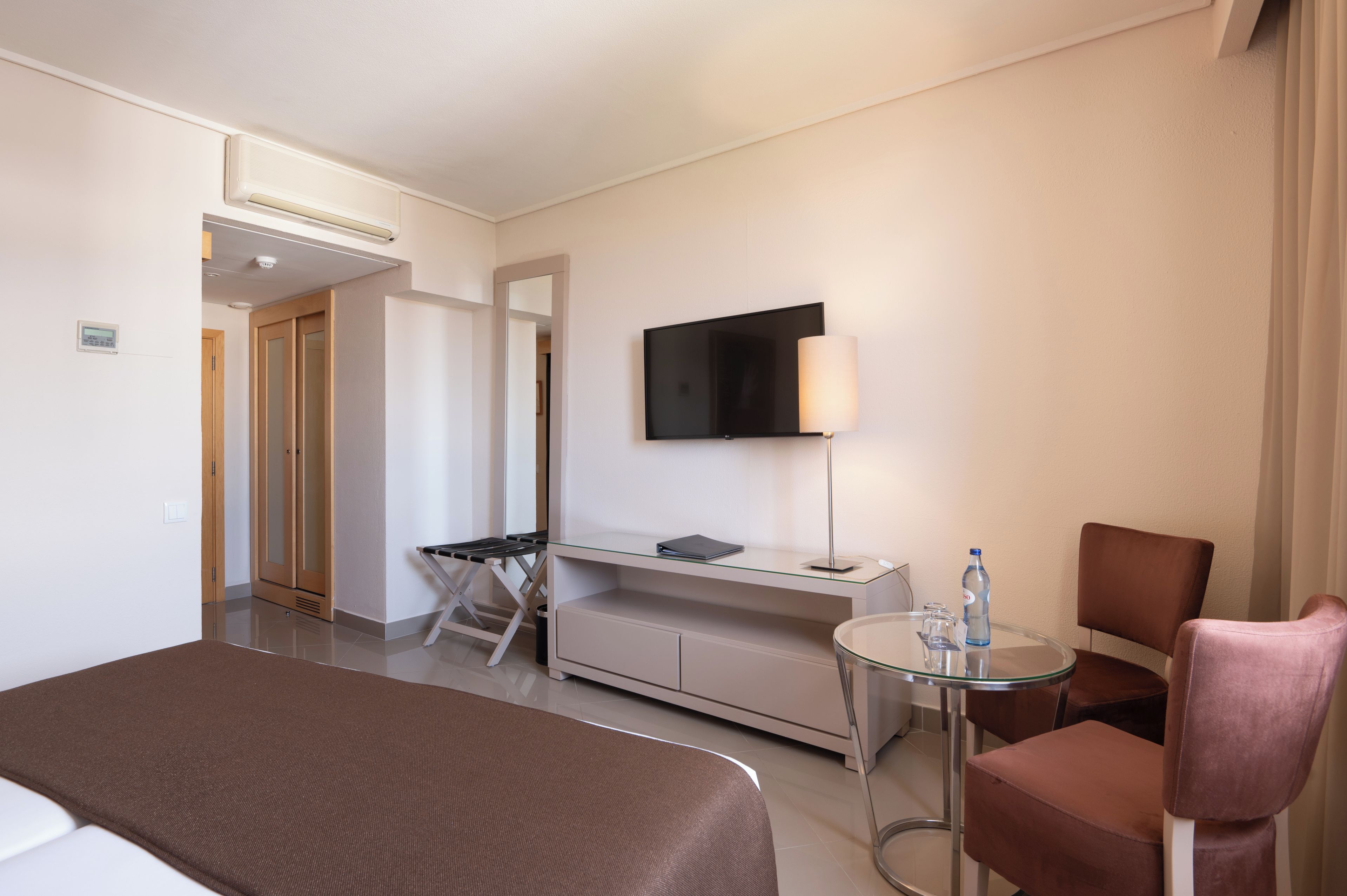 A hotel room with a bed, a desk, a chair, a television, and a small table.