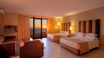 A hotel room with a bed, a desk, a chair, a TV, and a view of the ocean.