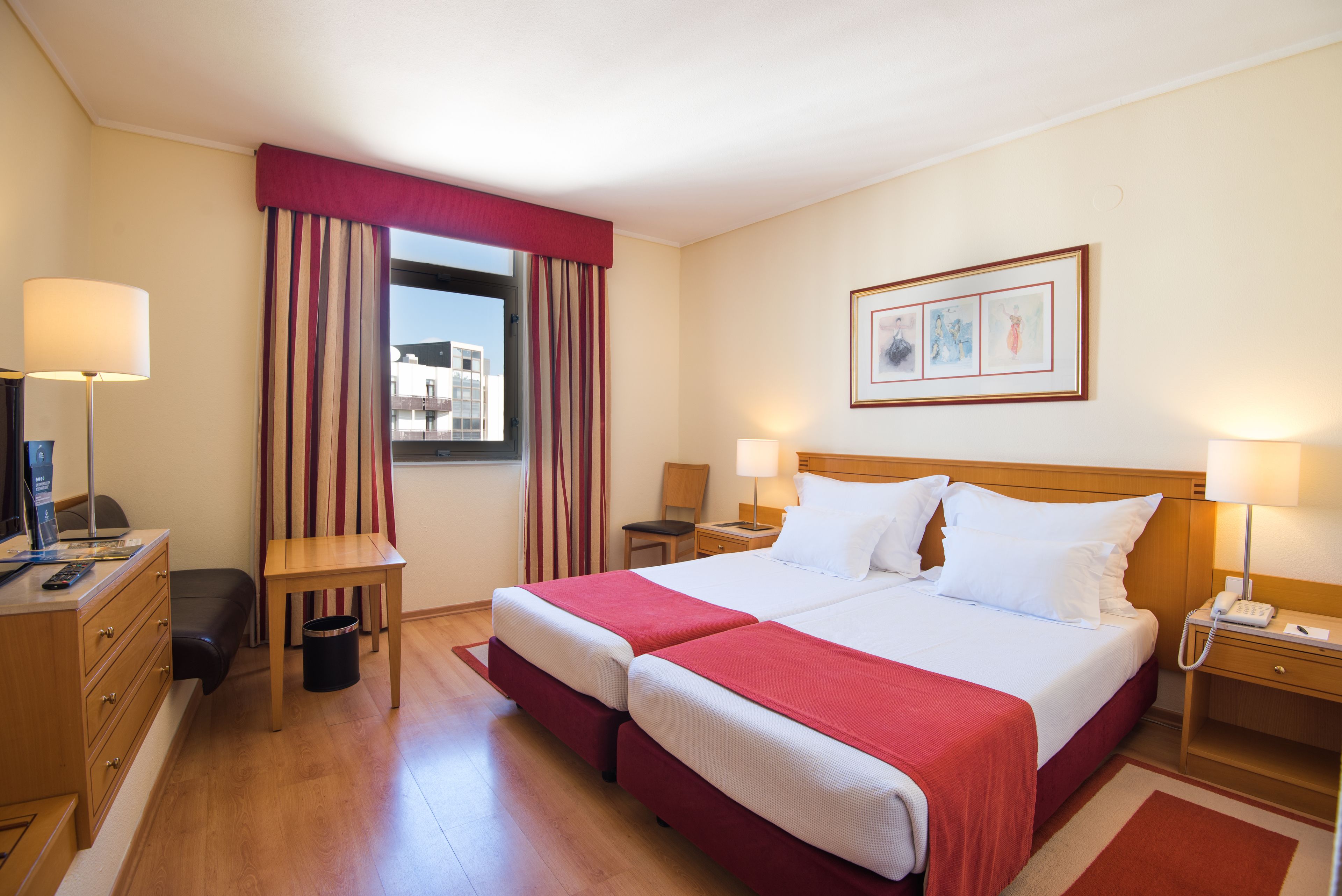 A hotel room with two beds, a desk, a chair, a lamp, a telephone, and a window with curtains.