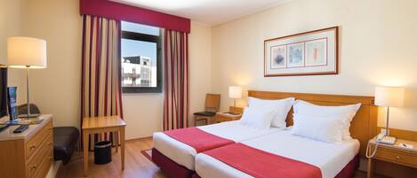 Habitación de hotel con dos camas, un escritorio, una silla, una lámpara, un teléfono y una ventana con cortinas.
