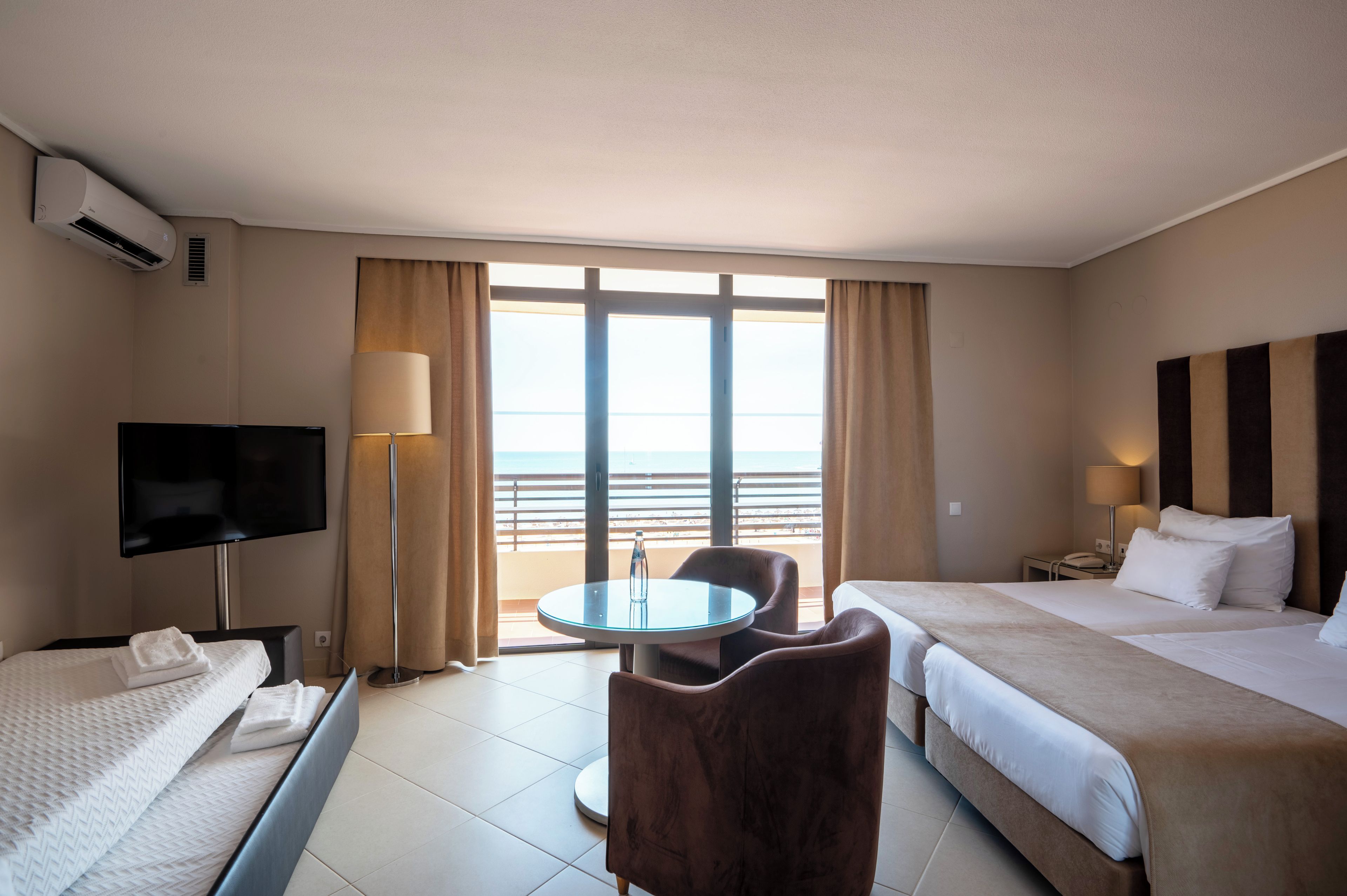 A hotel room with a bed, a TV, a desk, a chair, and a balcony with a view.