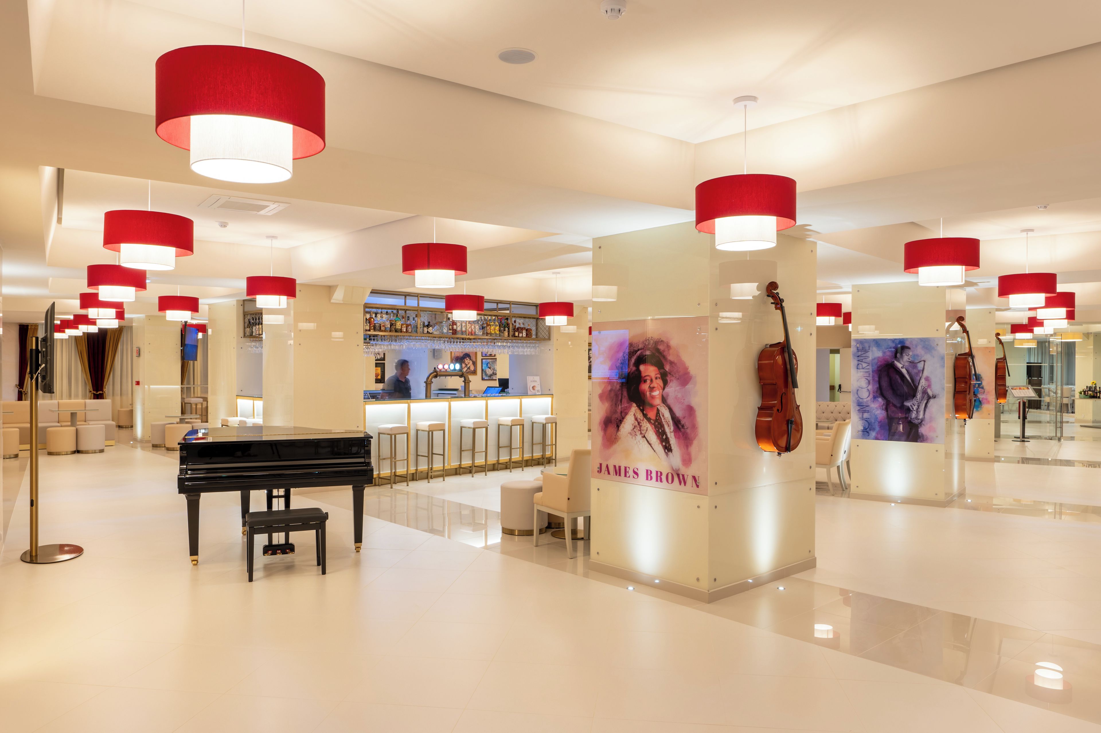 A modern lobby with a grand piano, red pendant lights, and a bar area.