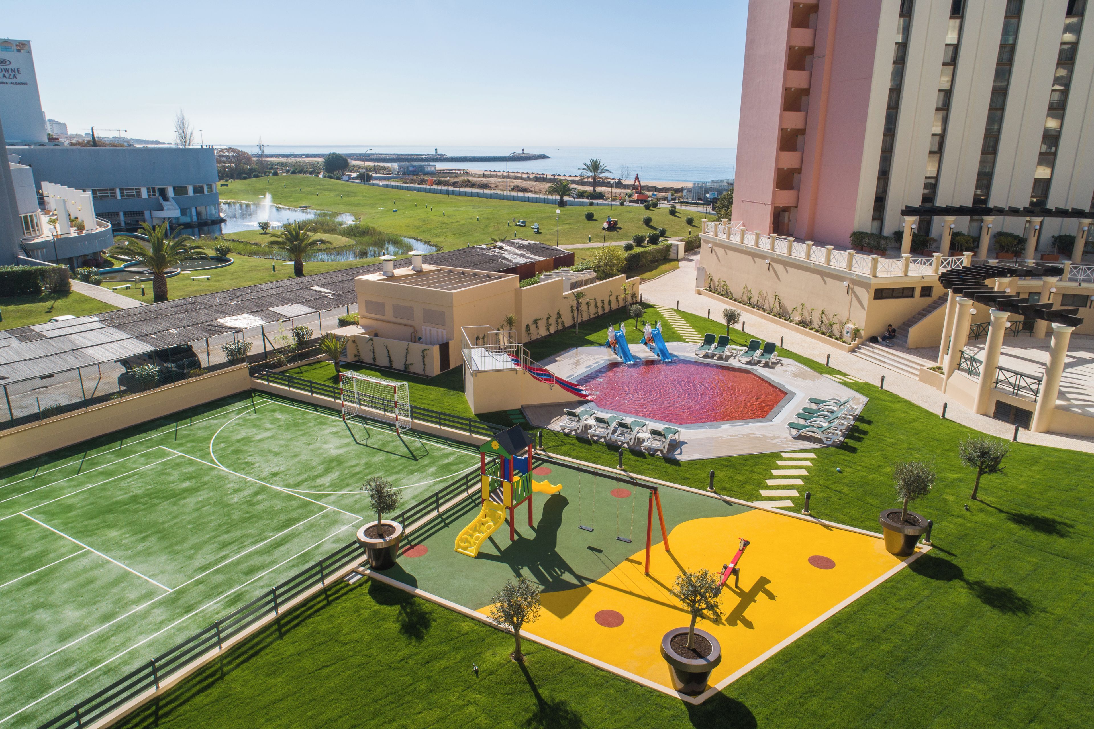Eine Dachterrasse mit Sportanlagen, darunter ein Tennisplatz, ein Spielbereich für Kinder und ein Schwimmbad.