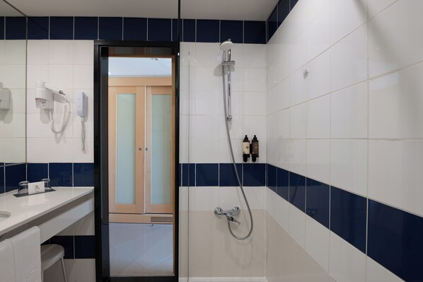 Un baño con ducha, tocador con espejo y secador de pelo.