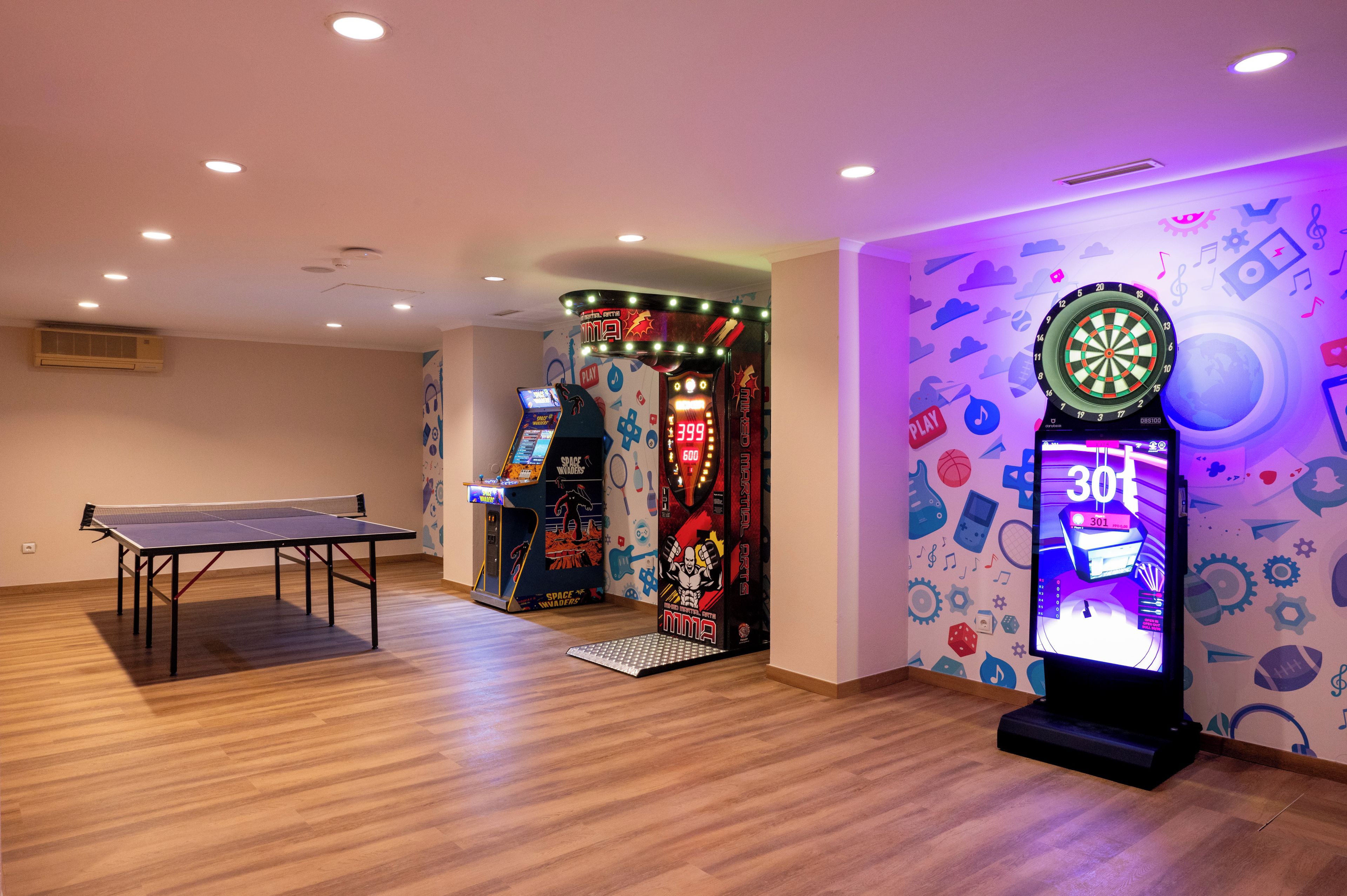 Una stanza con tavolo da ping pong, giochi arcade e bersaglio da freccette.