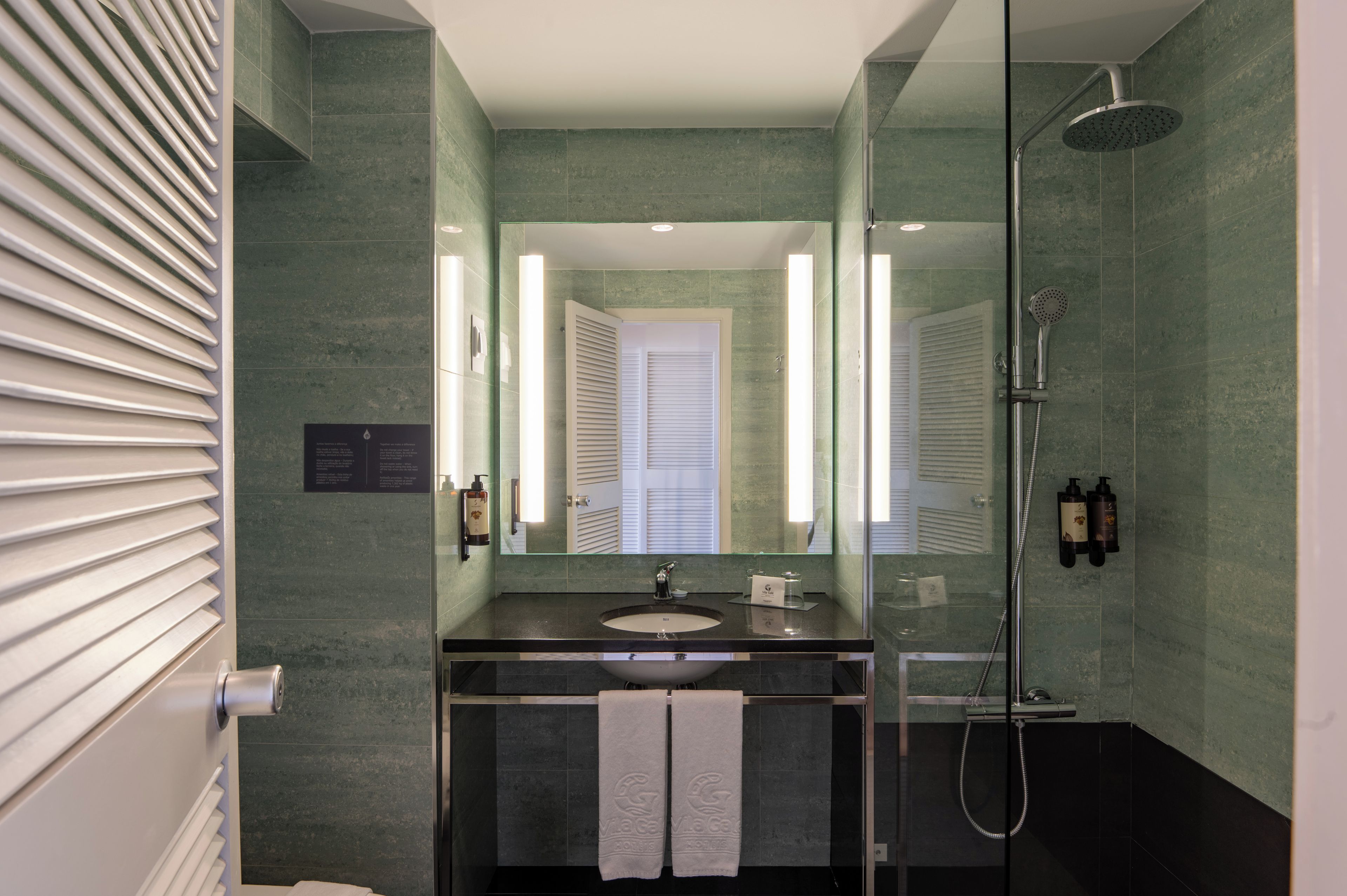 A modern bathroom with a glass shower enclosure, a sink with a mirror, and a towel rack.