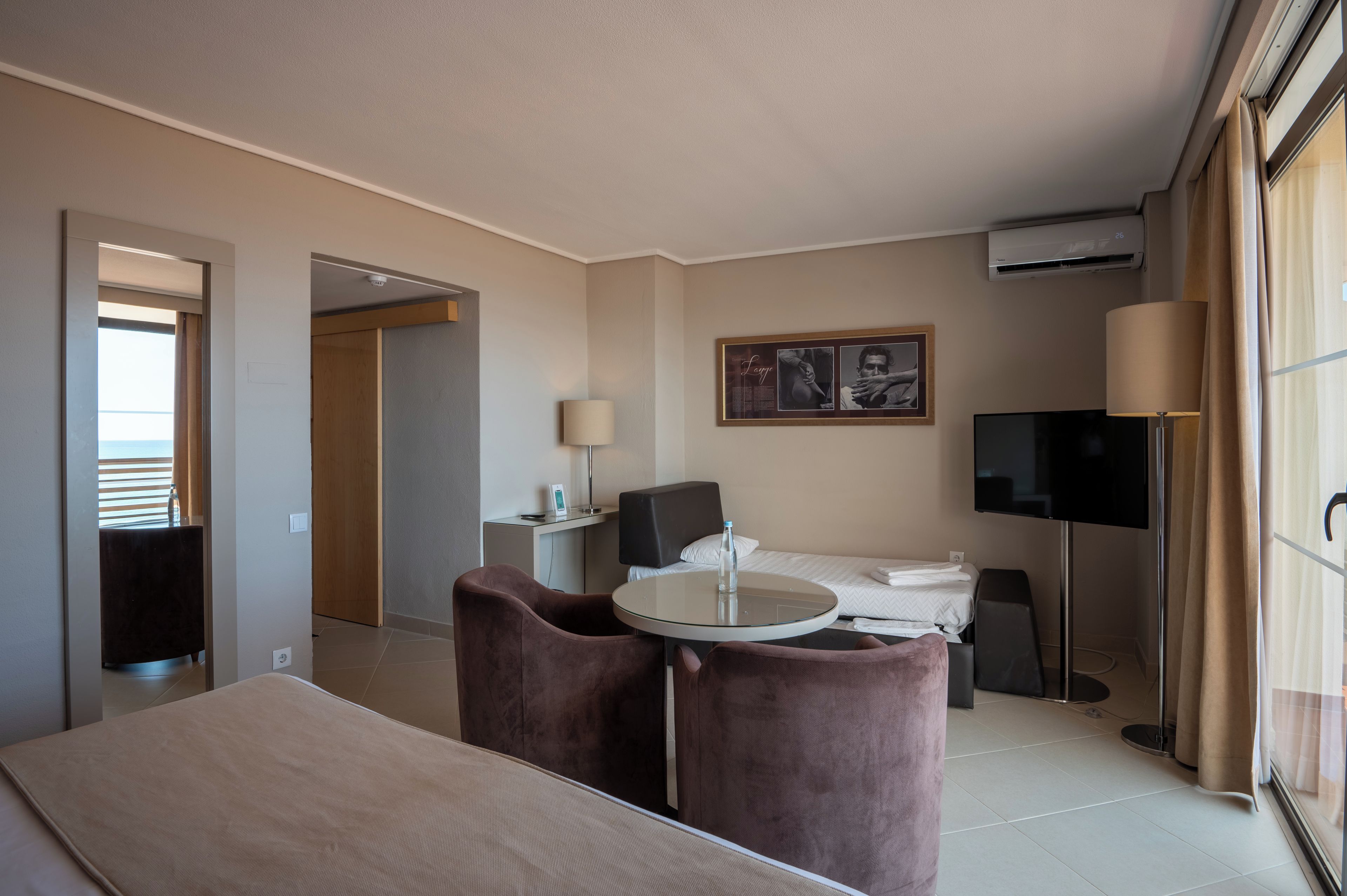 Habitación de hotel con cama, una mesita, dos sillas, televisor y ventana con cortinas.