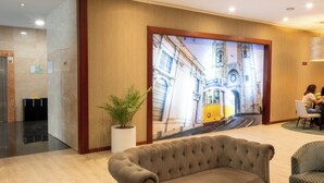 A lobby with a large mural of a train, a tufted sofa, and a reception desk. - VIP Executive Zurique Hotel (Lisbon)