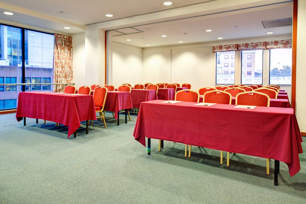 A conference room with multiple tables covered in red tablecloths, arranged in rows with orange chairs.