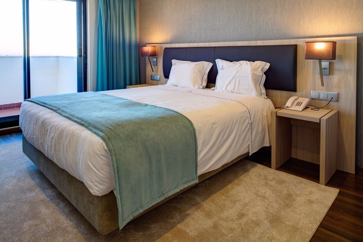 Habitación de hotel con cama, mesitas de noche, teléfono y ventana con cortinas.