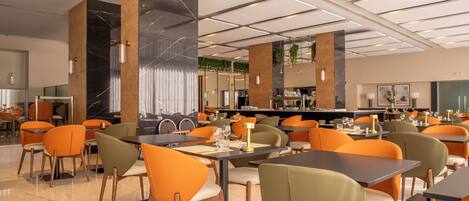 A modern restaurant with high ceilings, marble columns, and orange chairs. Tables are set with glasses and cutlery.