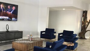 A modern living room with blue sofas, a wooden coffee table, and a flat-screen TV mounted on the wall.