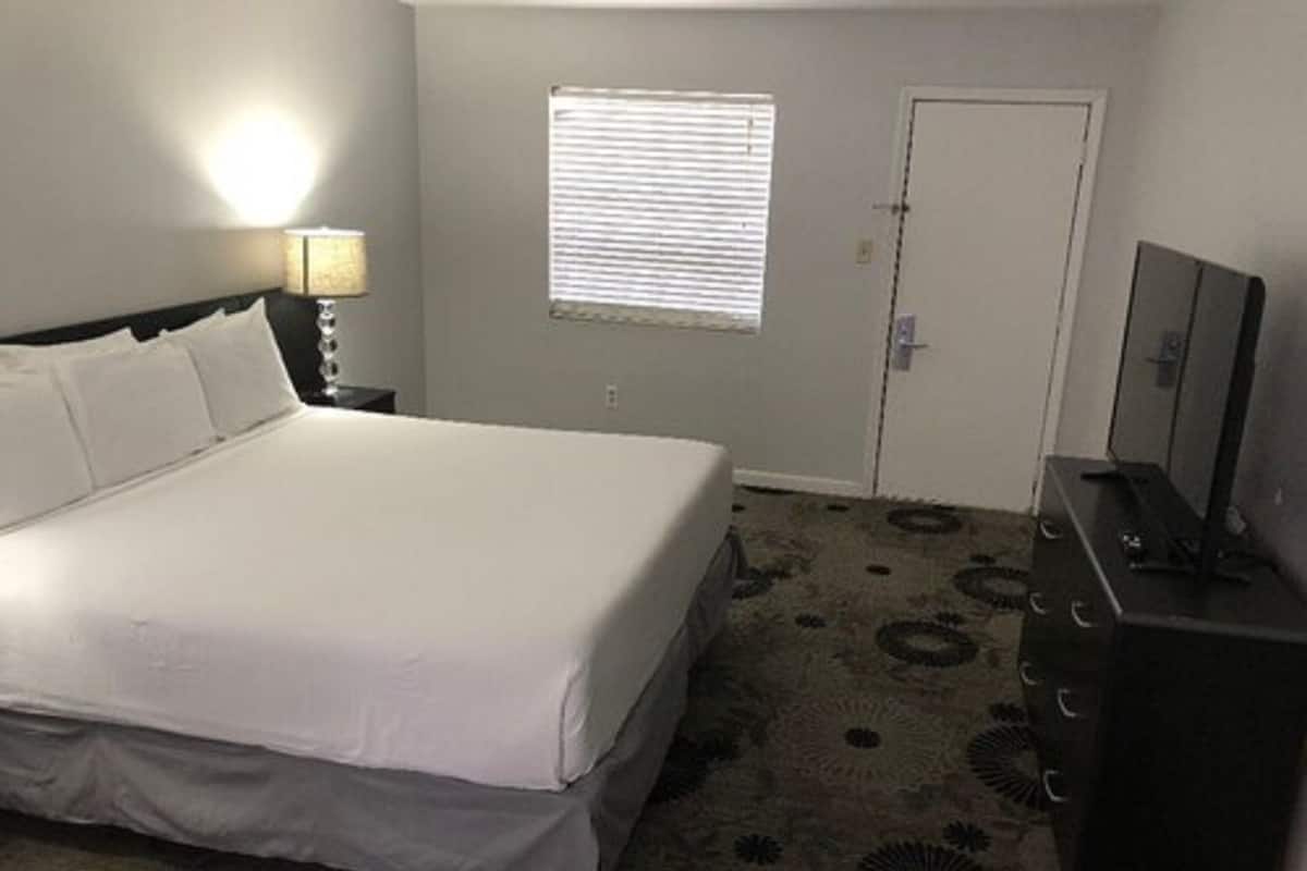 A hotel room with a bed, a dresser, a lamp, a window, and a door.