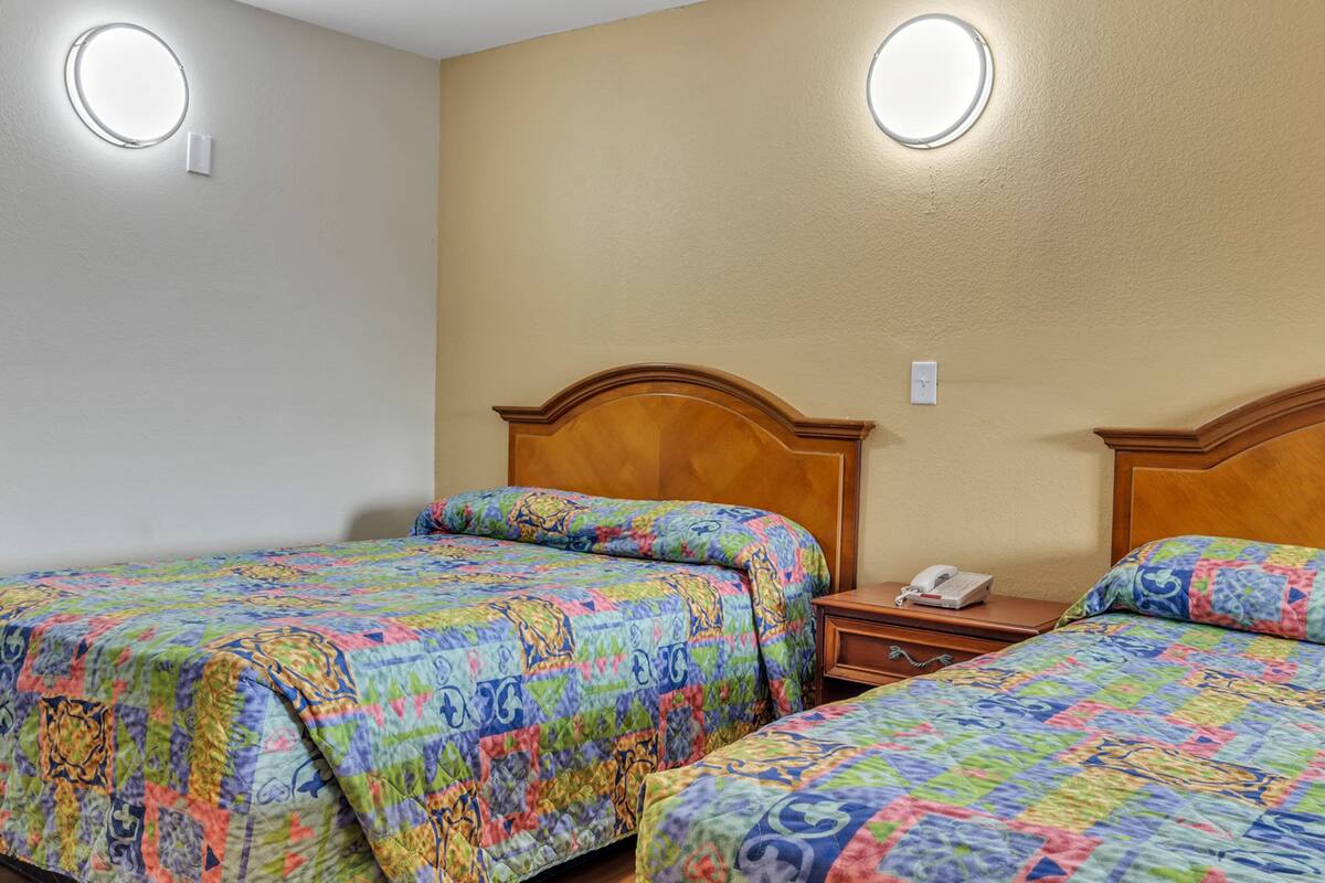 Hotellihuone, jossa on kaksi erillistä sänkyä, puinen pääty, yöpöytä, jossa on puhelin, ja seinään kiinnitetty valaisin.