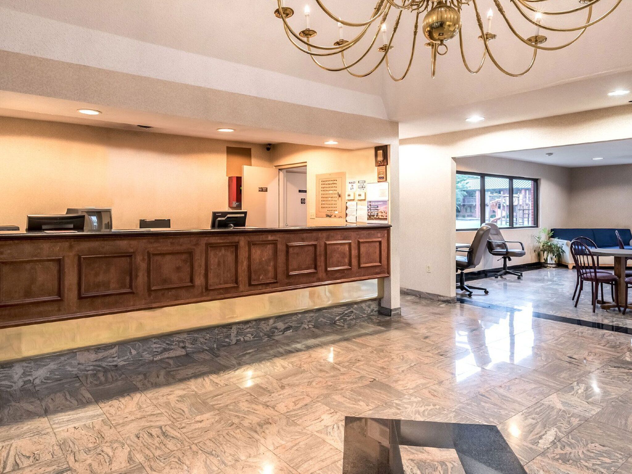 A reception area with a marble floor, a wooden reception desk, a chandelier, and a seating area with a table and chairs.