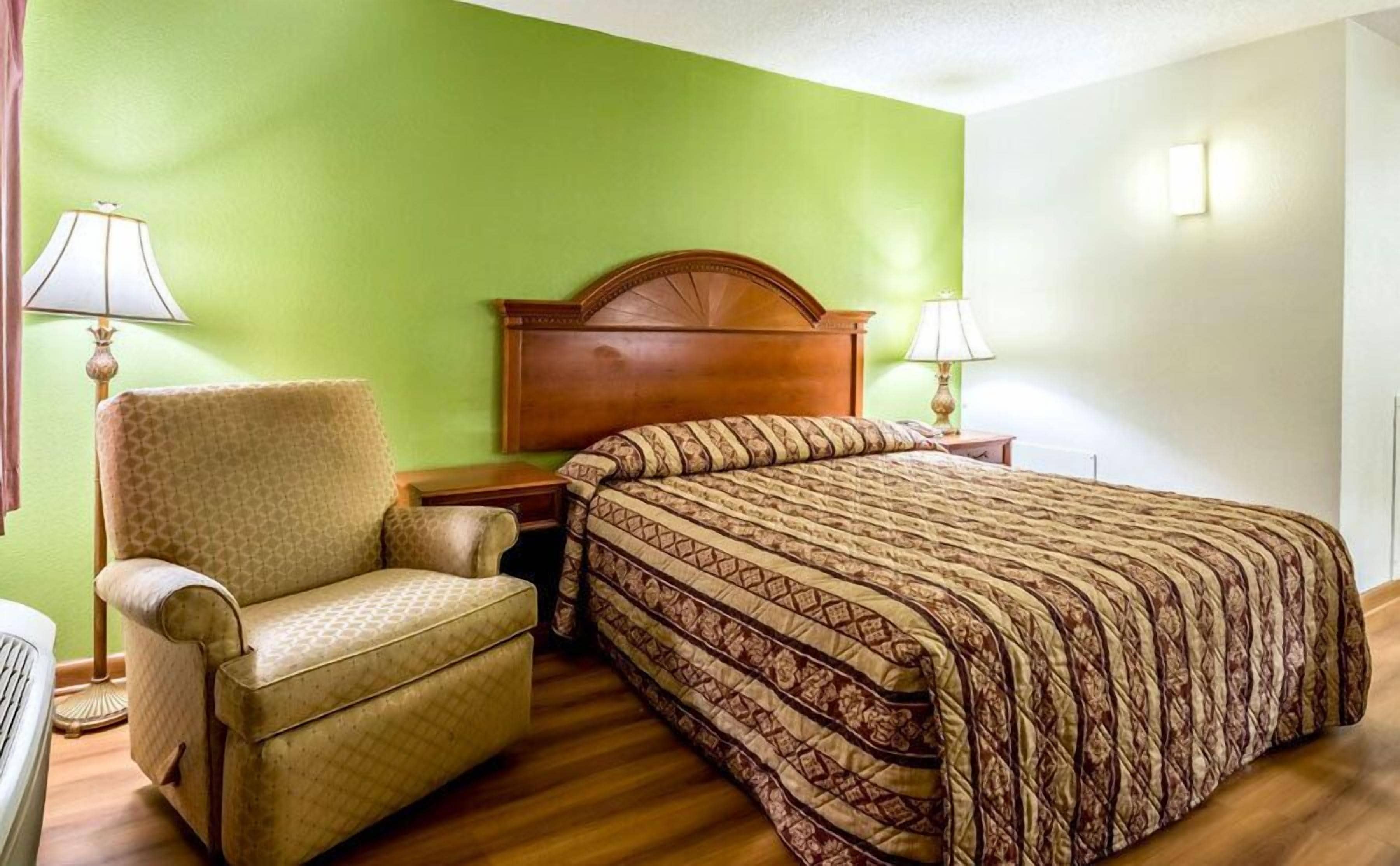 Une chambre d’hôtel avec un lit, une chaise, deux tables de chevet et une tête de lit en bois.