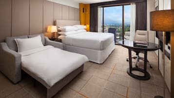 A hotel room with a large bed, a smaller bed, a sofa, a desk, and a view of the city.
