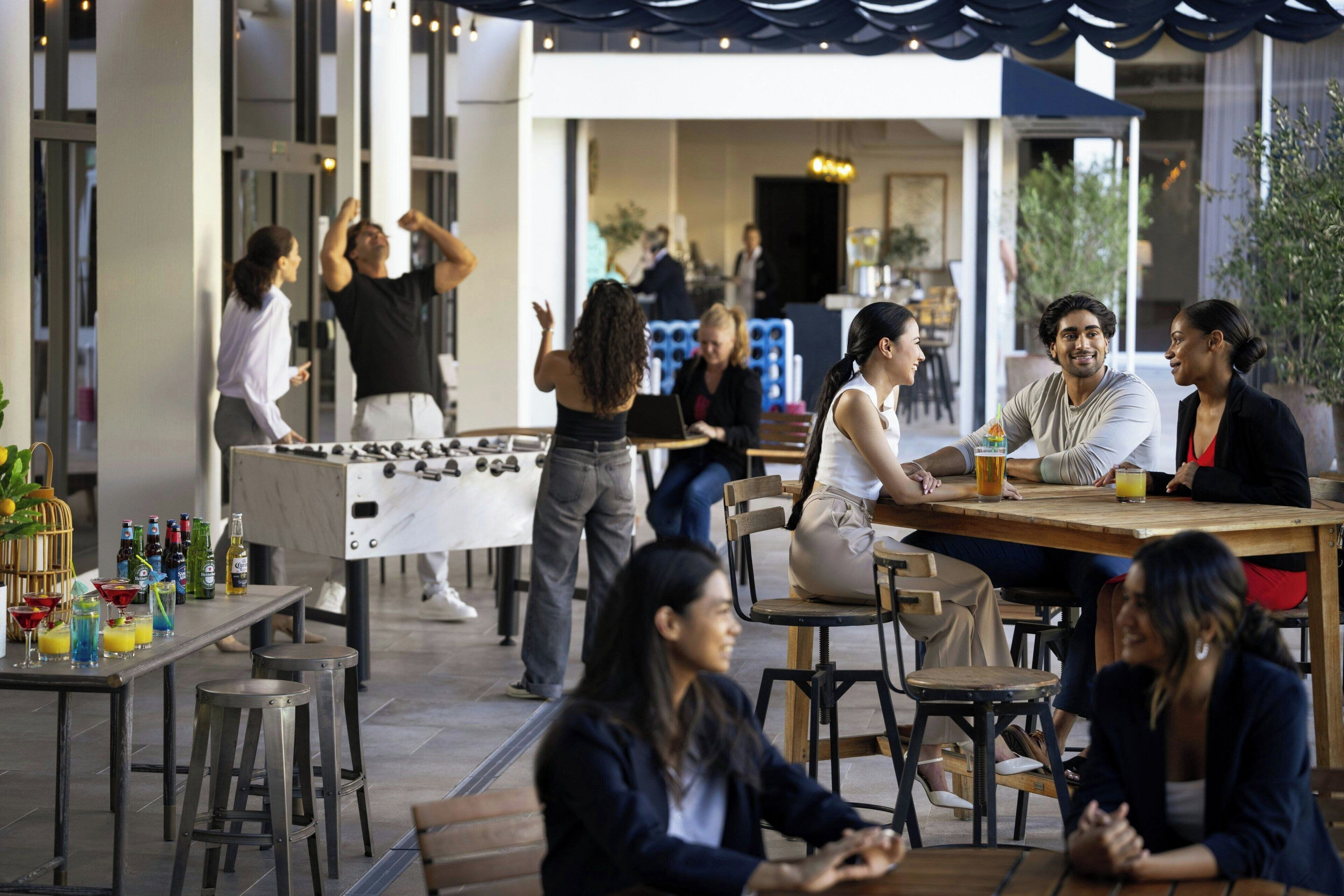 An outdoor dining area with tables and chairs, a foosball table, and a bar with stools.