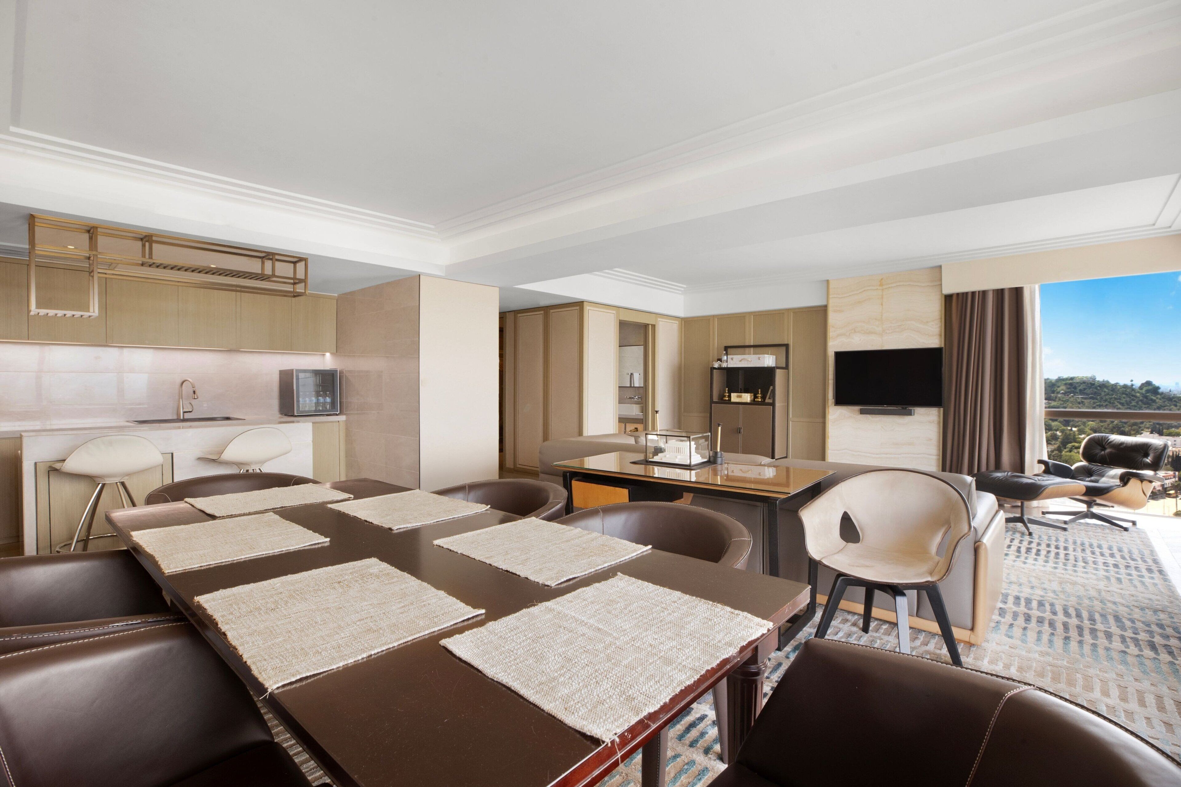 A hotel room with a dining area, a kitchenette, a flat-screen TV, and a view of the outdoors.