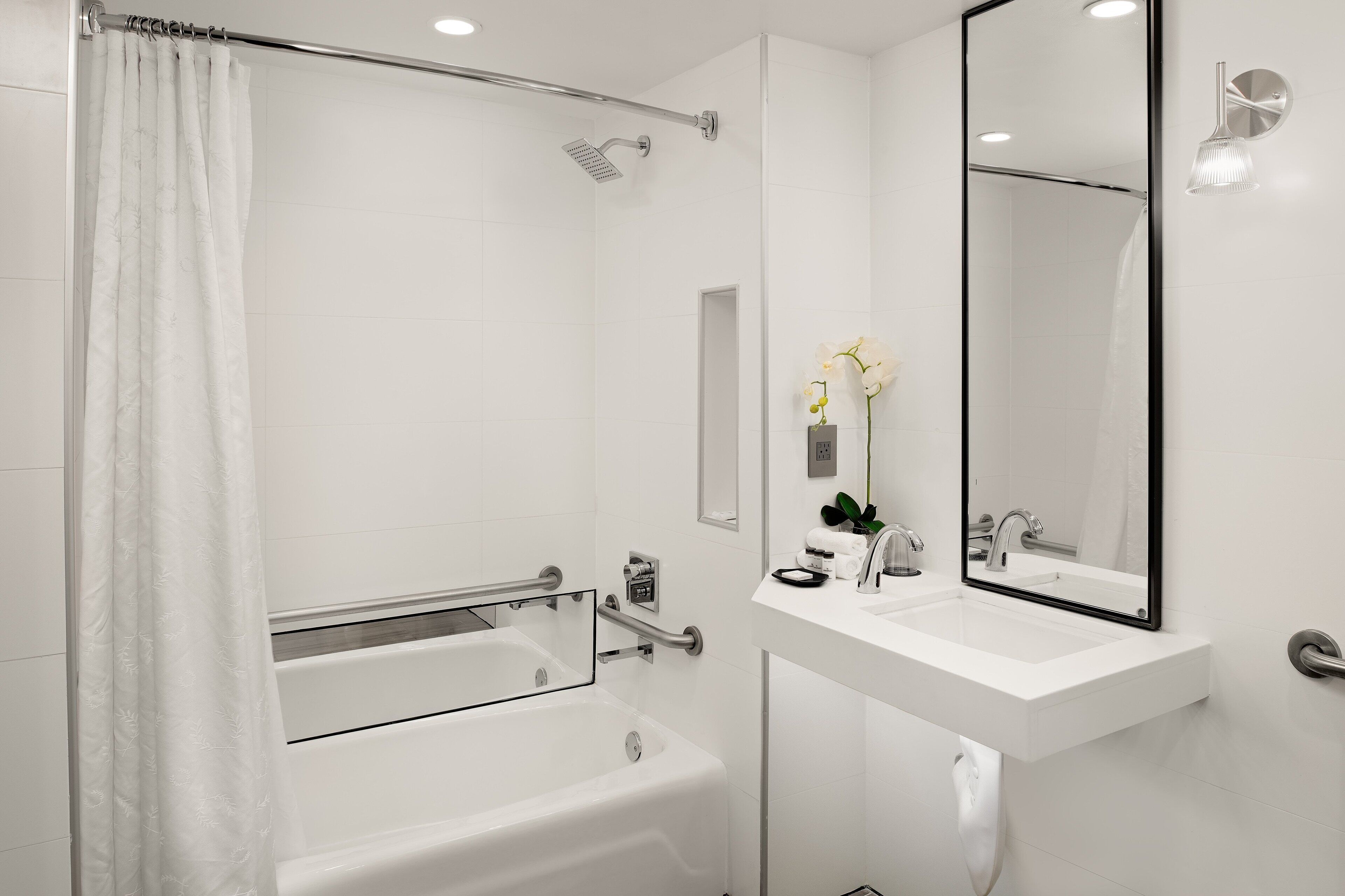 A modern bathroom with a bathtub, shower, and a large mirror above the sink.