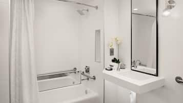 A modern bathroom with a bathtub, shower, and a large mirror above the sink.
