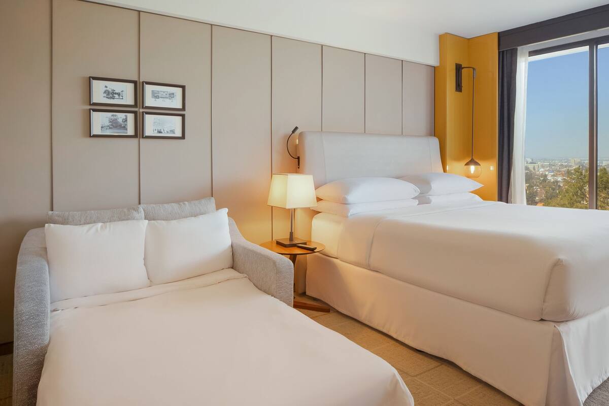 A hotel room with two beds, a nightstand, a lamp, and framed pictures on the wall.