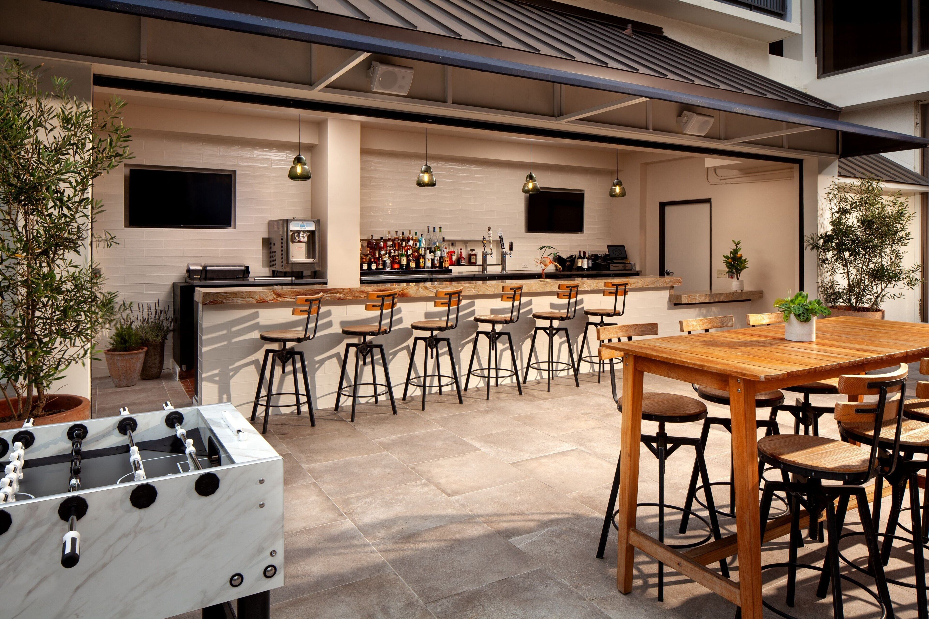 Zona de bar moderna con una mesa de fútbol de mesa, taburetes y una barra con diversas botellas.