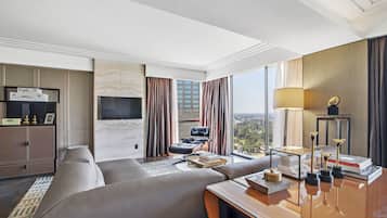 A modern hotel room with a large sofa, a desk with a lamp, a TV, and a view of the city.
