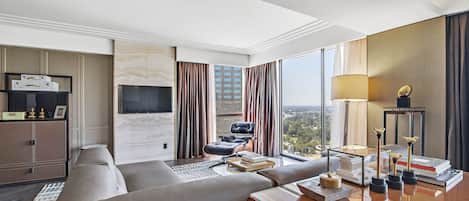 Habitación de hotel moderna con un sofá grande, un escritorio con lámpara, televisión y vistas a la ciudad.