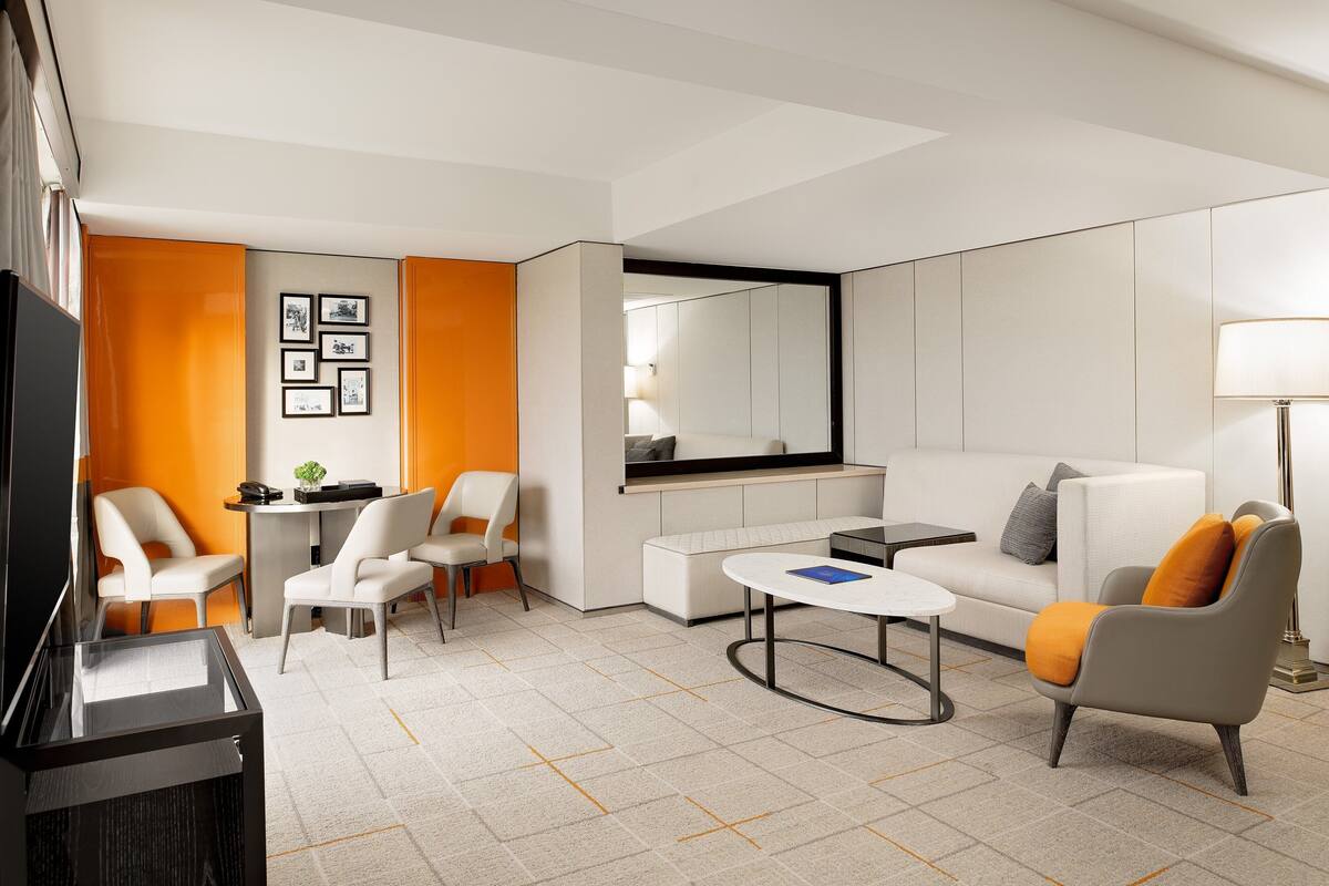 A modern living room with a sofa, armchairs, a coffee table, a TV, and a small table with a lamp.