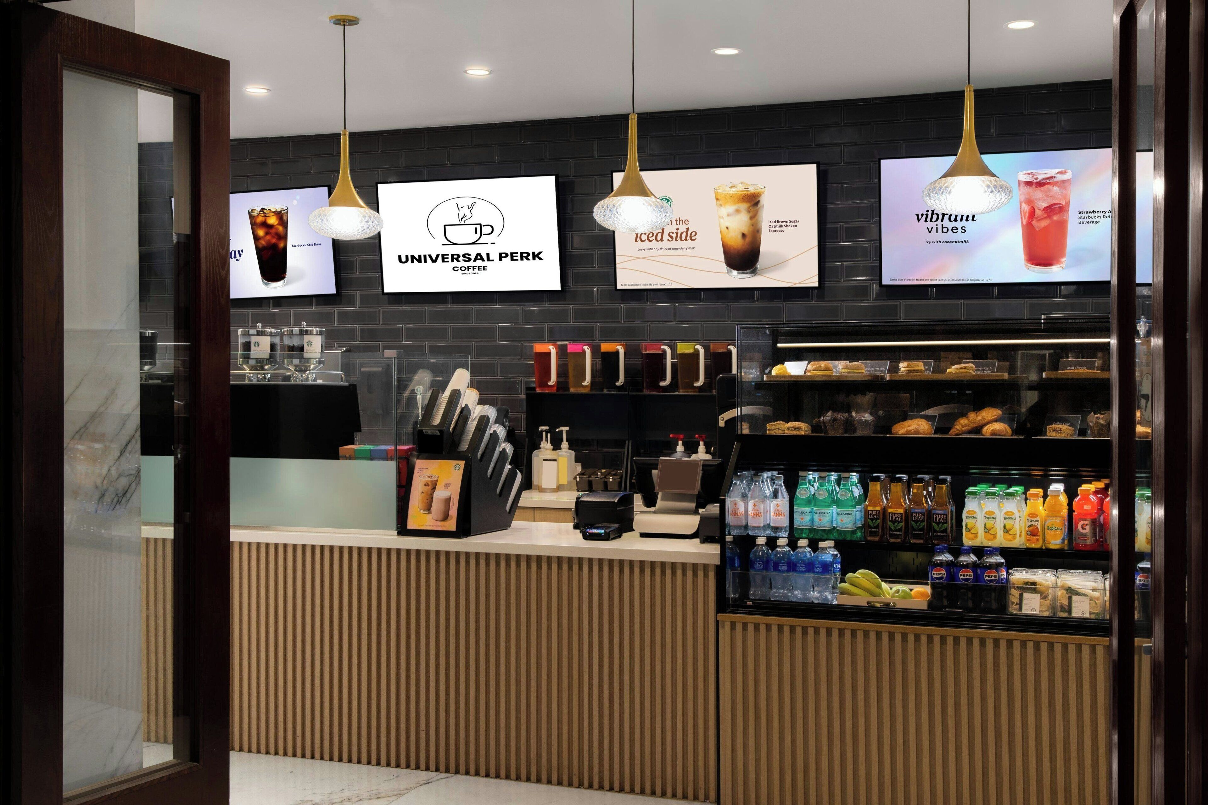 A modern coffee shop interior with a counter, beverage dispensers, and a refrigerated display of drinks.