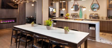 A modern kitchen with a central island, bar stools, a flat-screen TV, and a built-in oven.