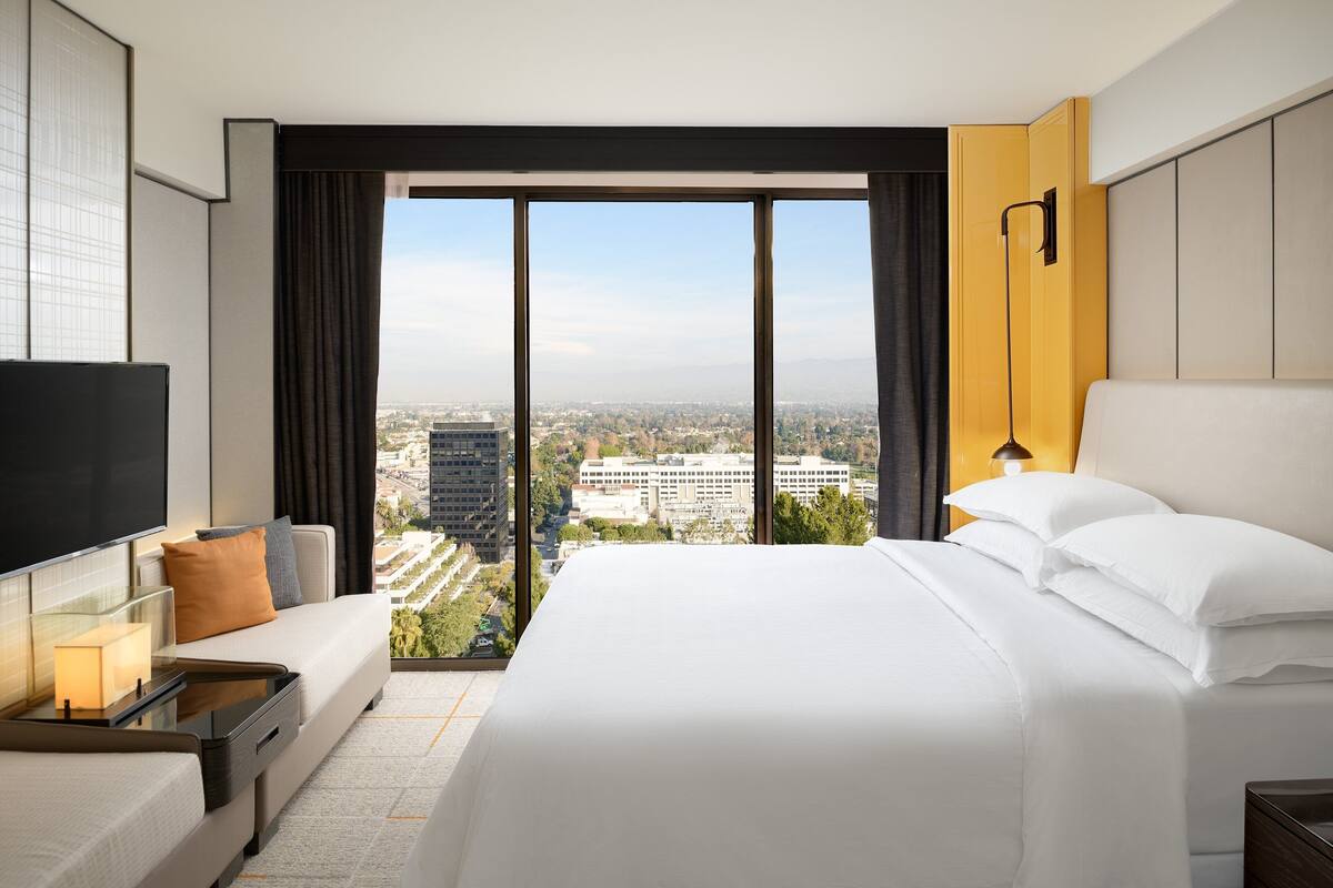 A hotel room with a large bed, a TV, a sofa, and a view of the city.