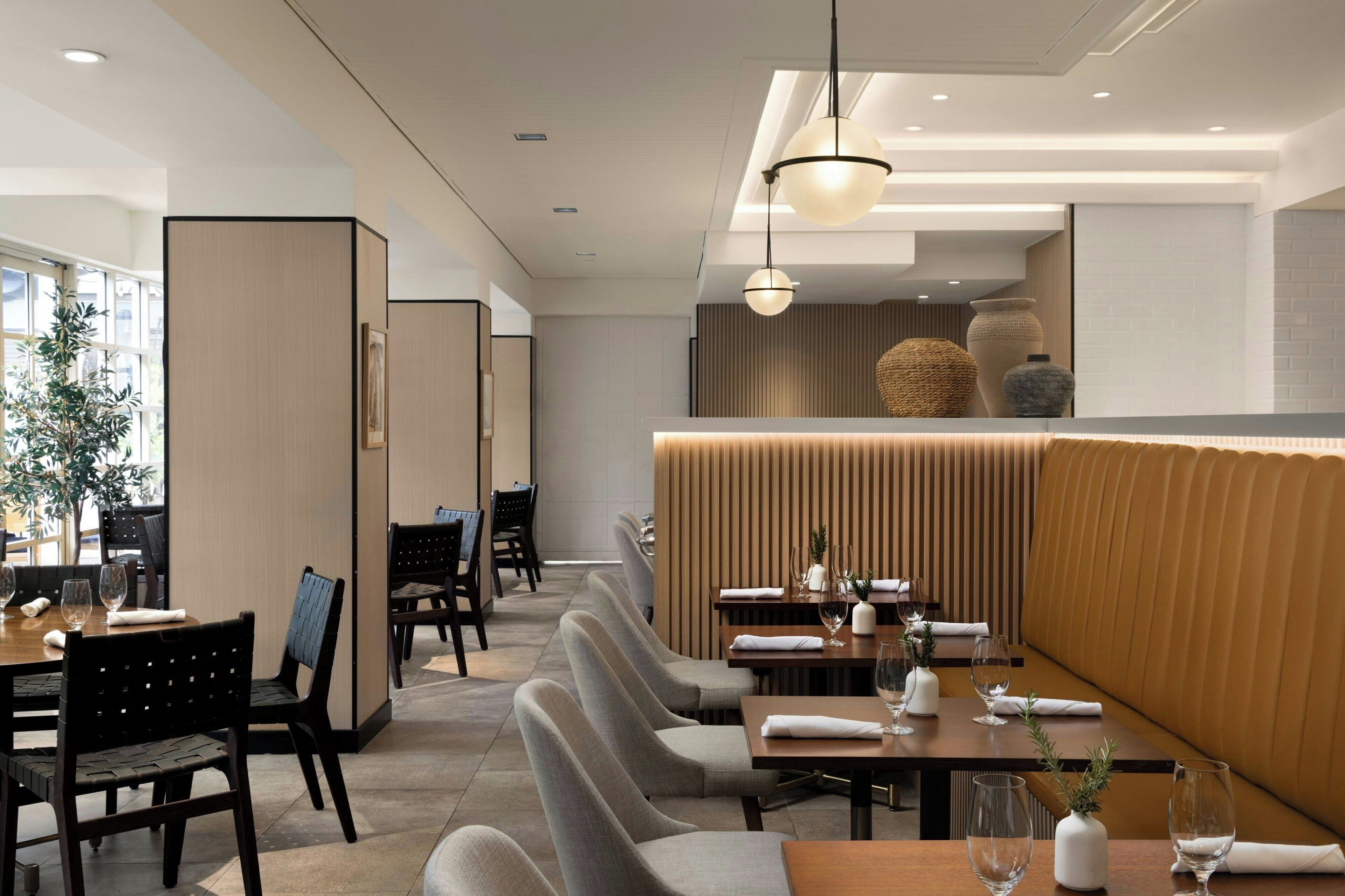 A modern restaurant with a long counter, booths, and a high ceiling with recessed lighting.