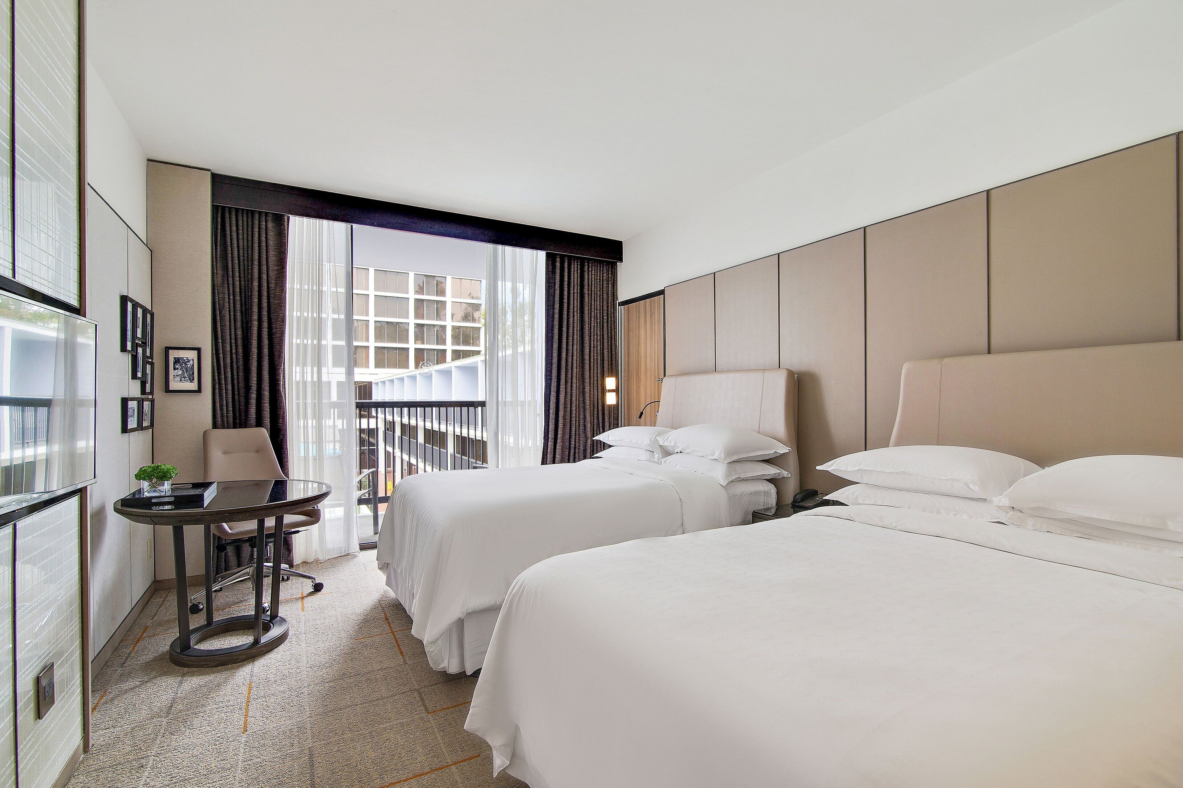 A hotel room with two beds, a small table, and a chair.
