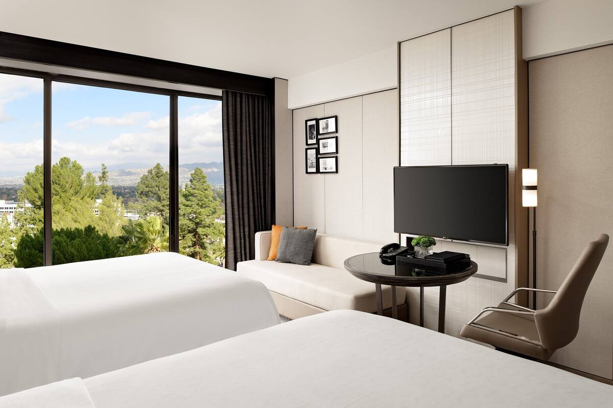 A hotel room with two beds, a sofa, a TV, and a desk with a phone and a plant.