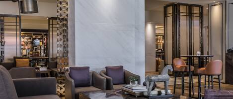 Een moderne lobby met lederen banken, een marmeren bijzettafeltje en een bar op de achtergrond.