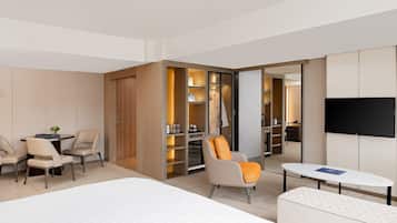 A modern hotel room with a bed, a seating area with chairs, a small table, a wardrobe, and a television.